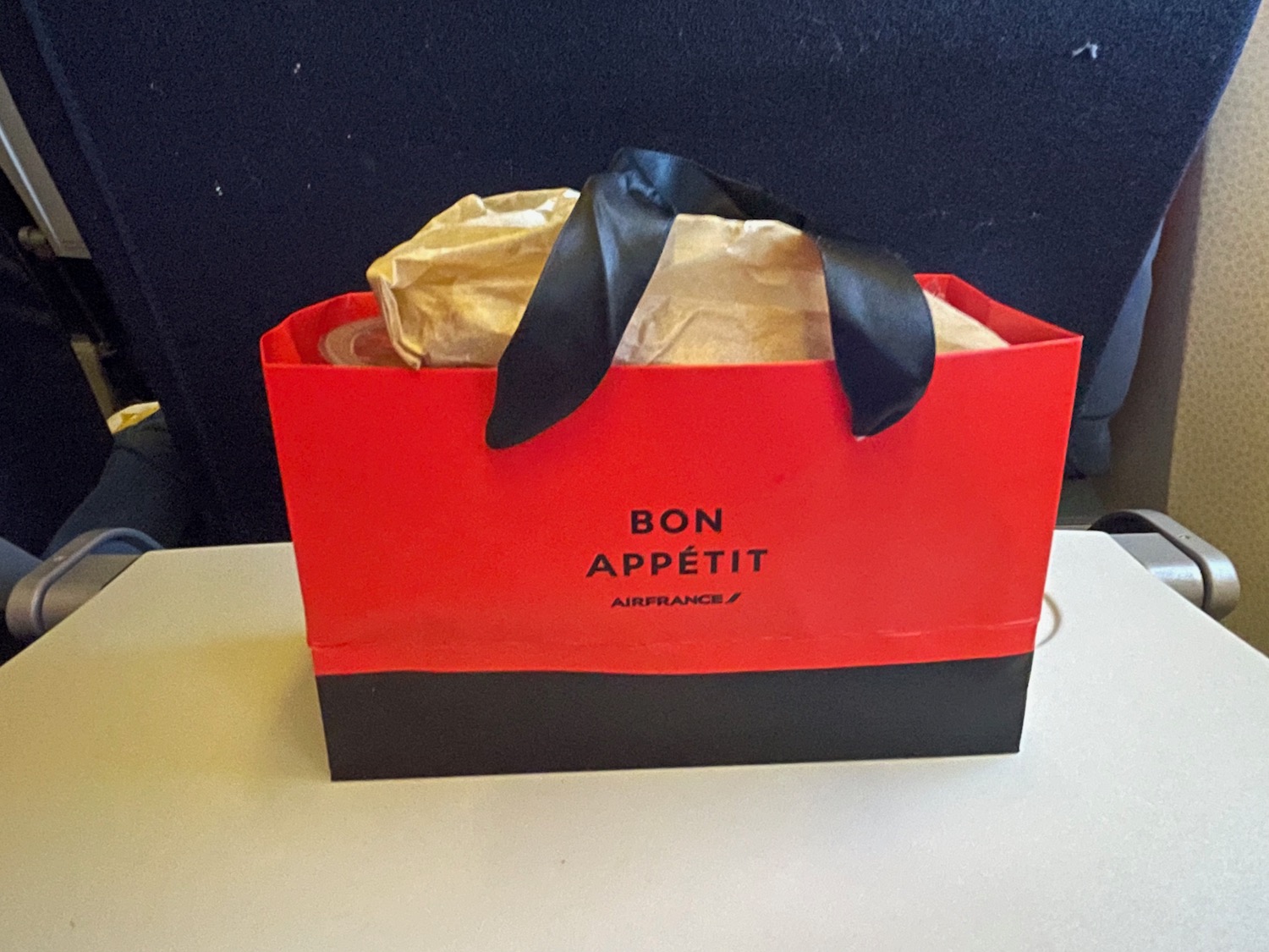 Red and black Air France meal box labeled "BON APPÉTIT" on an airplane tray table, showcasing in-flight dining experience in Economy Class.