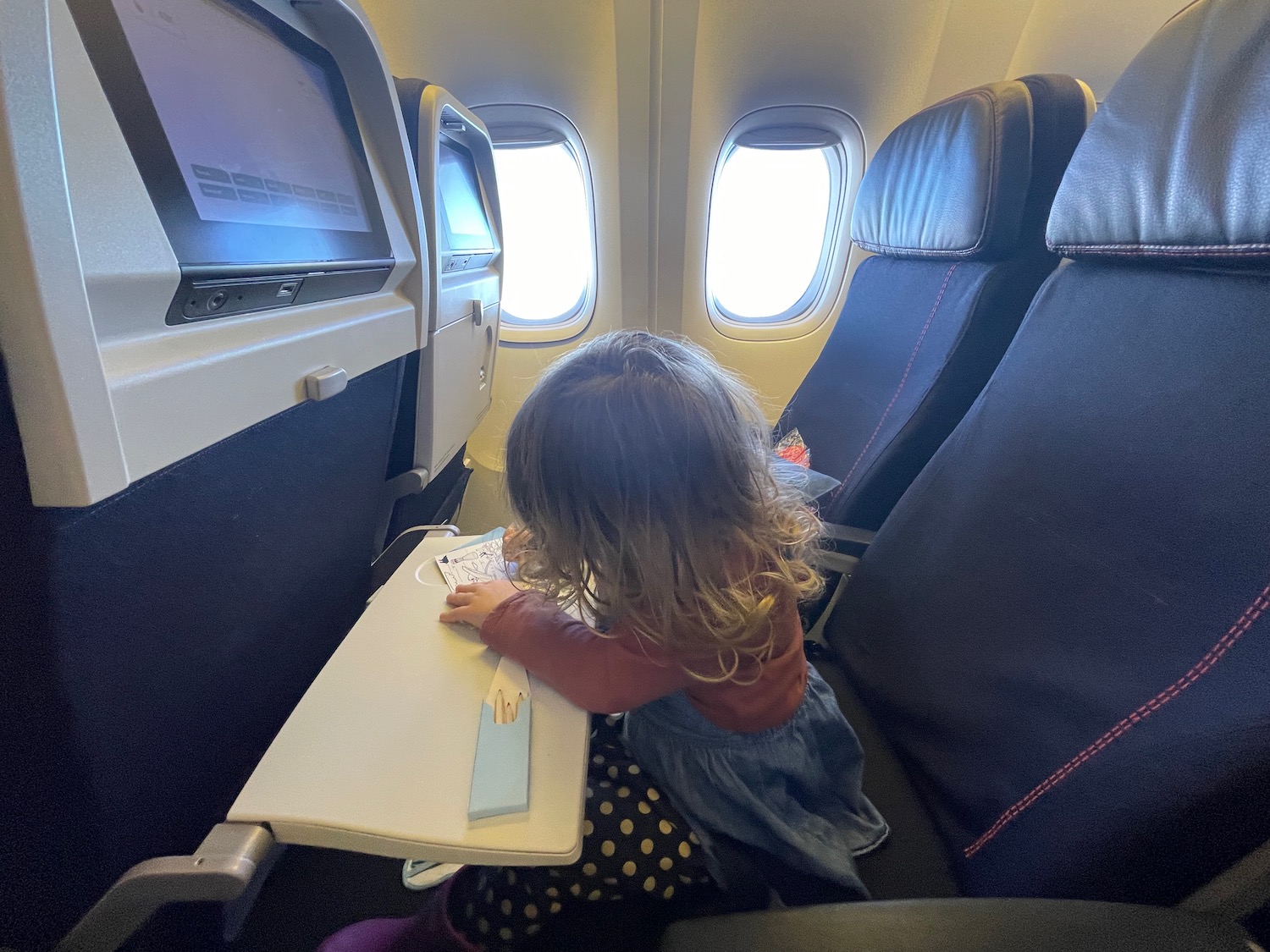 Child coloring on tray table in Air France 777-300ER Economy Class, with in-flight entertainment screens and window view.