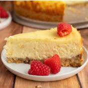 a close up of Gluten-Free Pecan Crust Cheesecake on a white plate with red raspberries