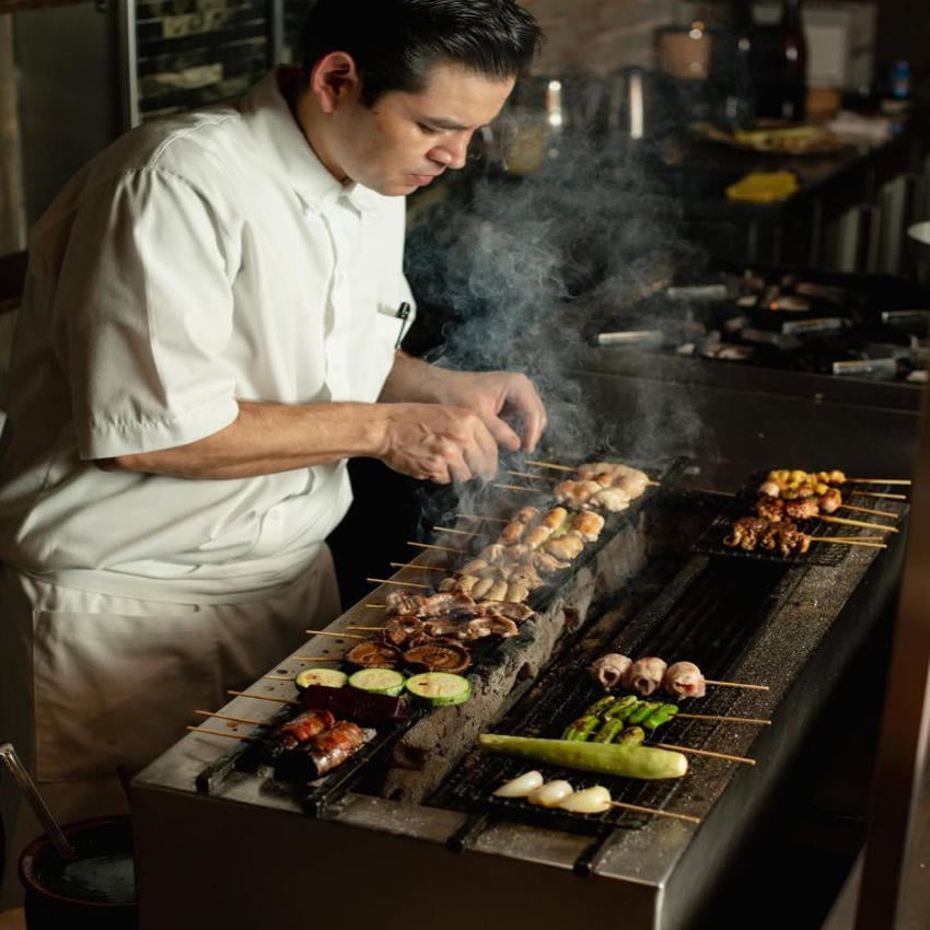 A chef prepares Japanese yakitori, grilling skewers of seafood, meat, and vegetables over a robata grill at a fine dining restaurant in Mexico.