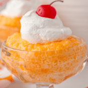 orange fluff salad in a glass dish topped with whipped cream and a maraschino cherry