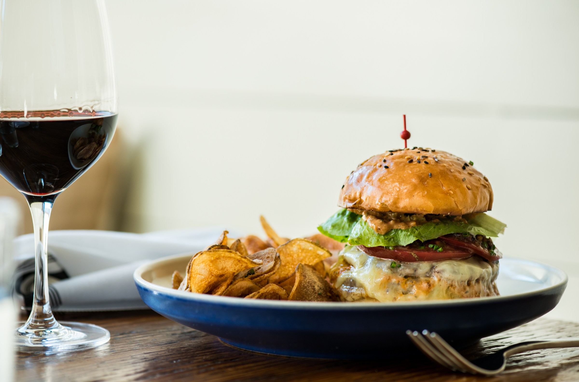 A burger oozing cheese with a side of potato chips and a glass of red wine at RT Bistro.