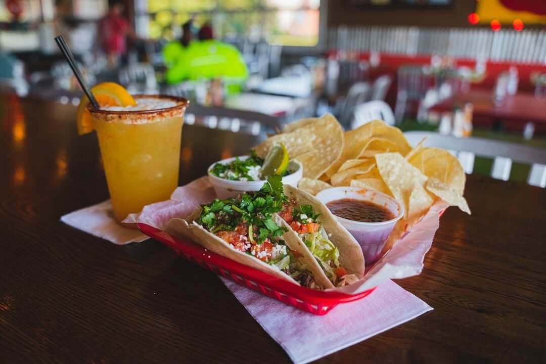 7 Beloved BHAM Restaurants We'll Miss - 4 A basket of tacos with chips, salsa, guacamole, and a margarita garnished with an orange slice sits on a wooden table at Taco Mama.