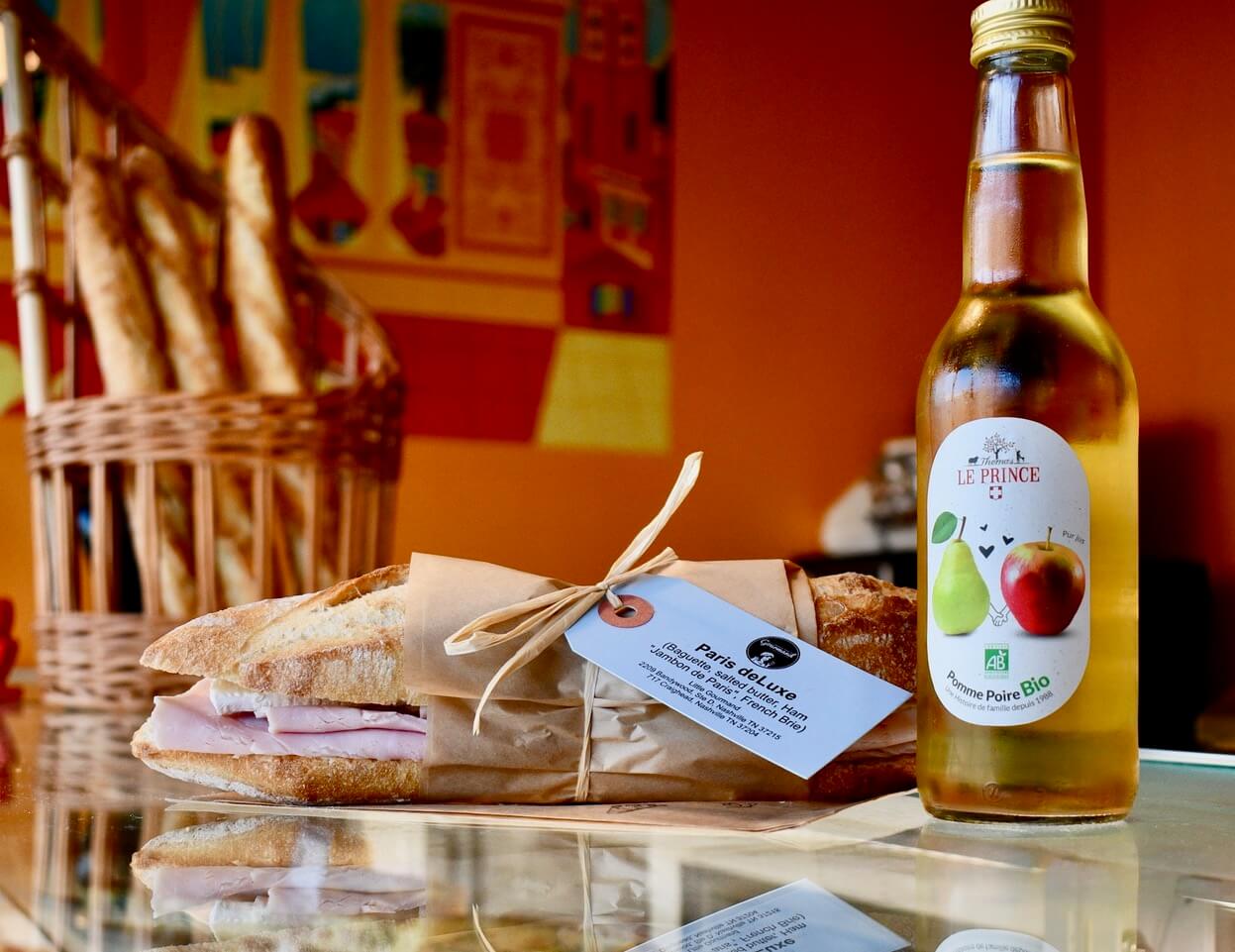 A French sandwich on a baguette, with an apple and pear soda. 