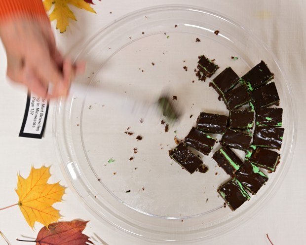 A hand shown reaching with a utensill toward a plate of chocolate mint brownies.