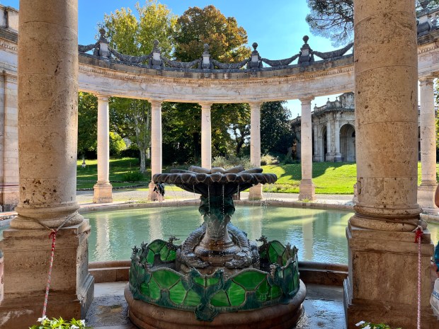 A fountain surrounded by green stained glass next to a pool that is surrounded by marble pillars