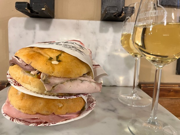 Sandwiches stacked up next to two glasses of wine