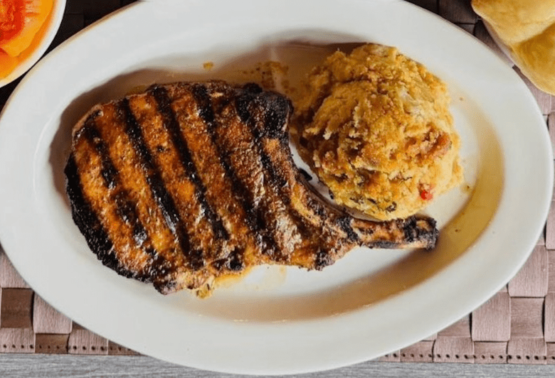 Over shot of a pork chop and a scoop of dressing on a white, oval-shaped plate. 