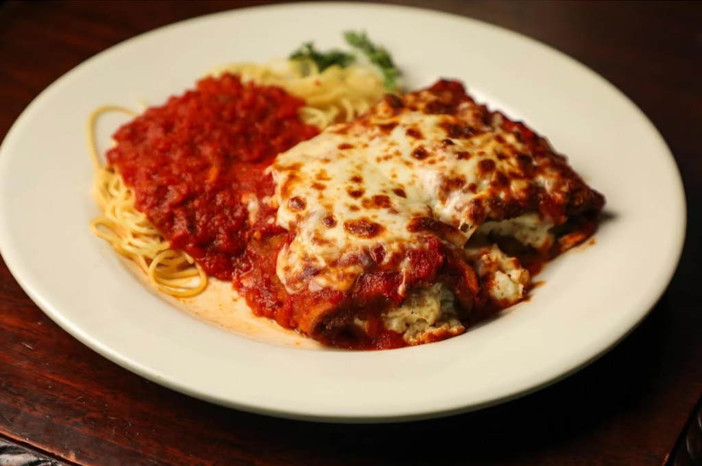 A plate of either veal or chicken parmesan. There is angel hair pasta with marinara on one side of the plate and the chicken or veal covered with sauce and cheese on the other side of the plate.