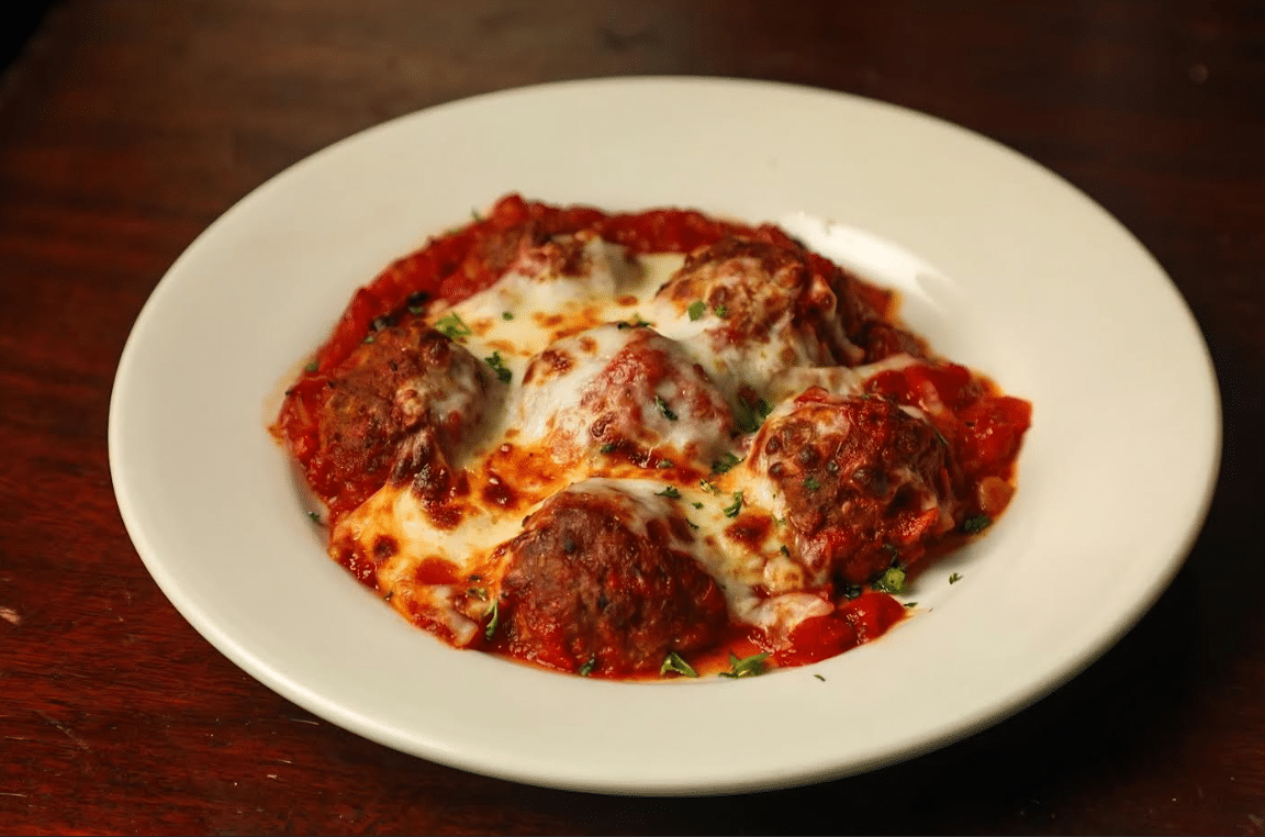 A plate of spaghetti and meatballs with melted cheese on top.