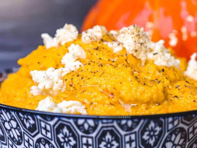 A bowl of mashed pumpkin topped with crumbled cheese and black pepper, with a decorative black and white pattern on the bowl.