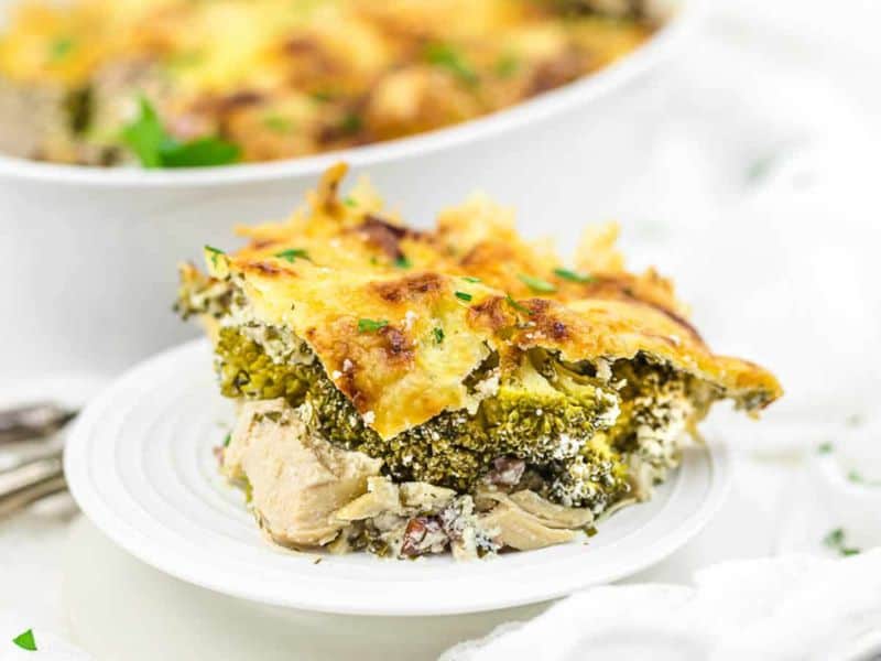 Shredded cooked chicken with red and green bell peppers in a sauce, served in a white dish with metal tongs and a spoon.