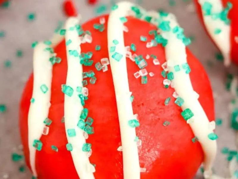 A round red cookie with white icing drizzles and green sugar sprinkles on top.