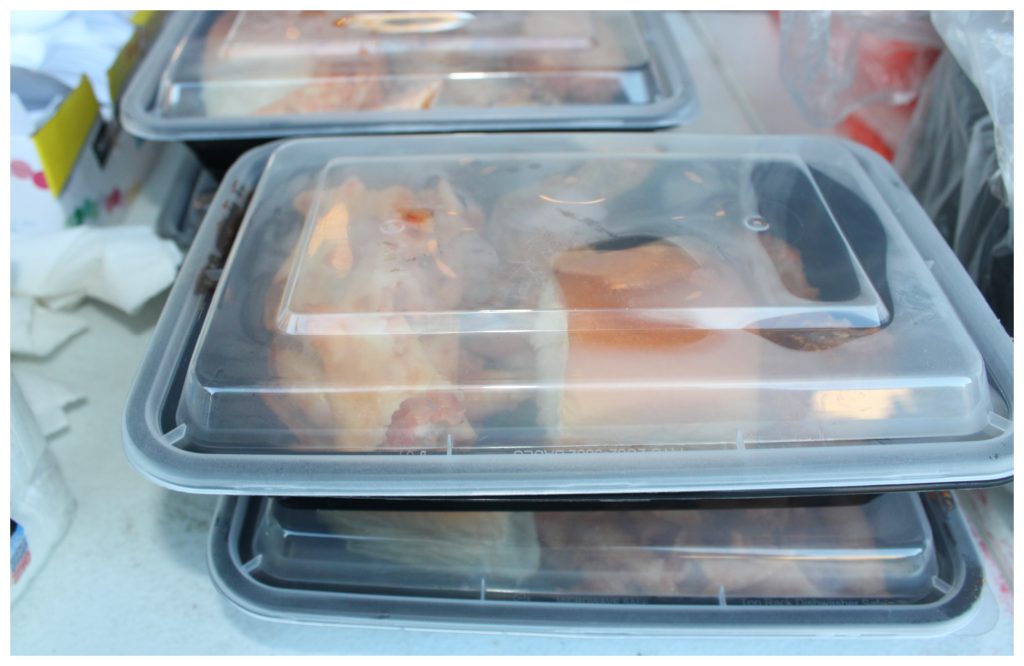 Food containers filled with chicken and mostaccioli are stacked on a table and ready to go to the 150 children and families in line at the MASK Peace Academy for food.