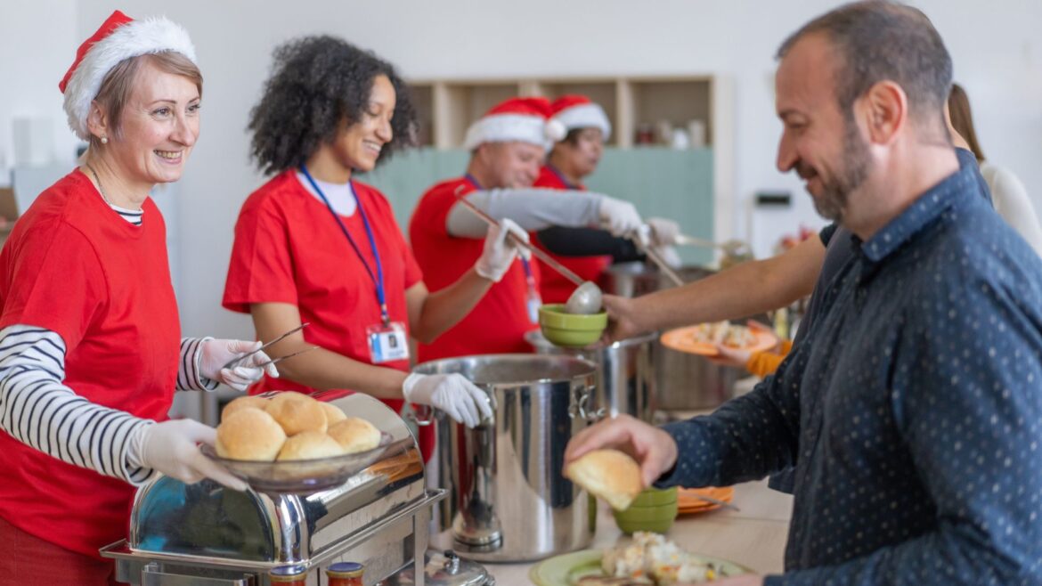 Soup kitchen volunteers serving food at Christmas, wearing Santa hats