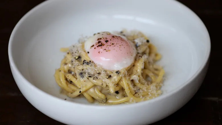 Spaghetti with poached egg and black pepper on top in white bowl