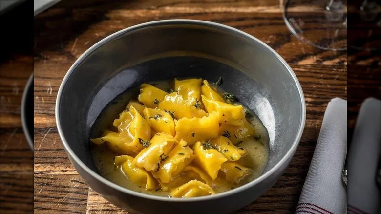 Plin pasta in buttery sauce with thyme in gray bowl on wooden table