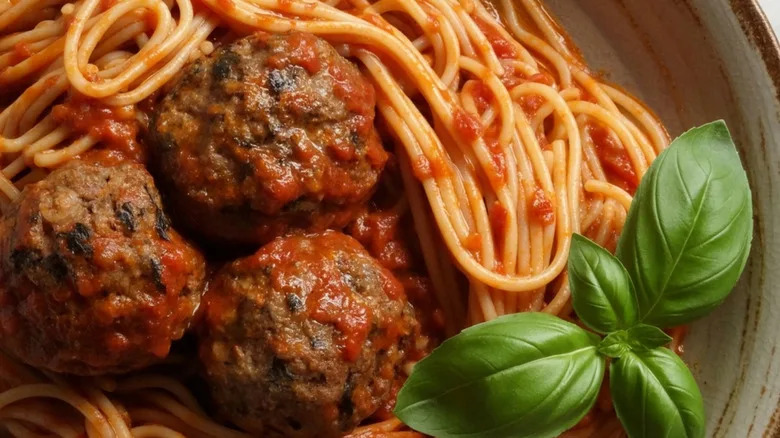 A closeup of a plate of spaghetti and meatballs with a sprig of fresh basil