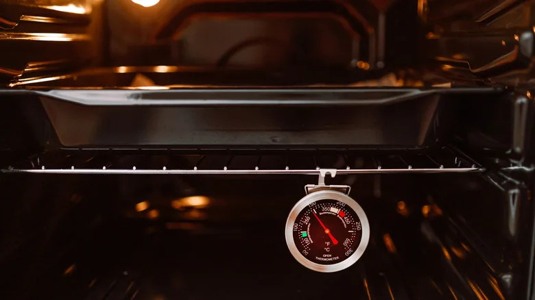 An oven thermometer hanging on an oven shelf with a baking pan