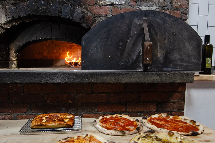 Wood-fired pizzas sit on a counter in front of a brick oven.