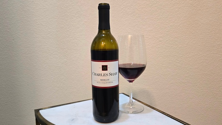 Charles Shaw merlot bottle and a glass filled with wine on a coffee table