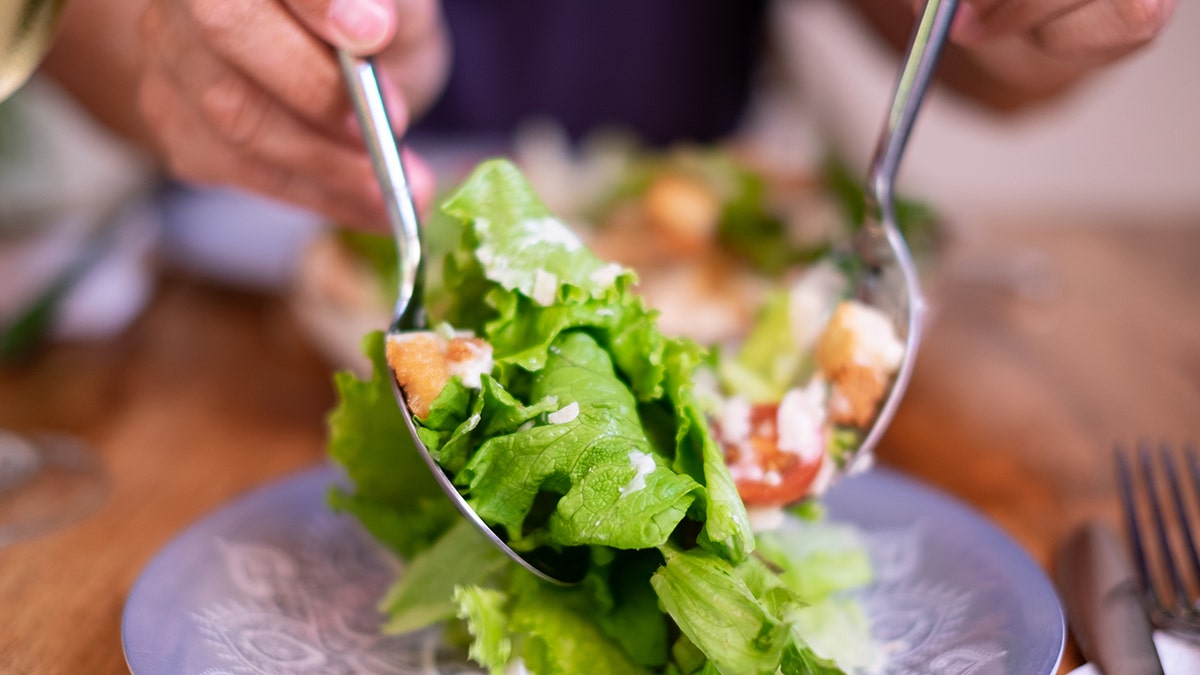 Caeser salad being plated at dinner table.