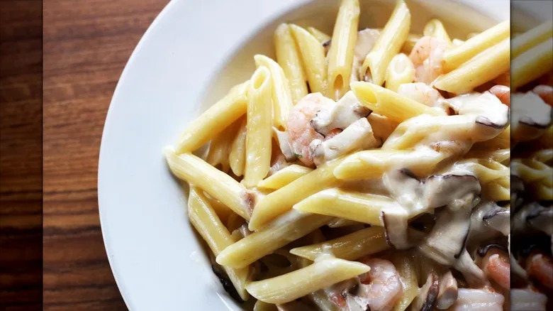 Penne with white sauce, mushrooms, and shrimp on white plate