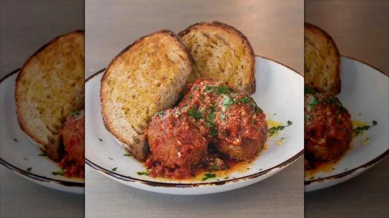 Meatballs topped with sauce next to sliced, toasted bread
