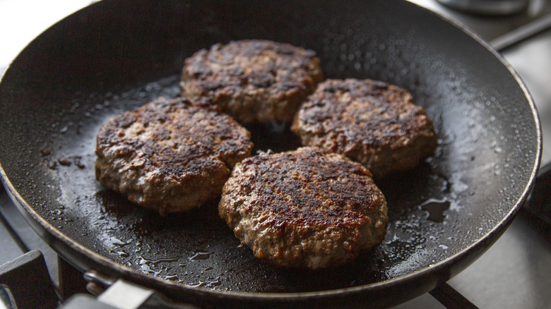 four hamburger patties in a black frying pan