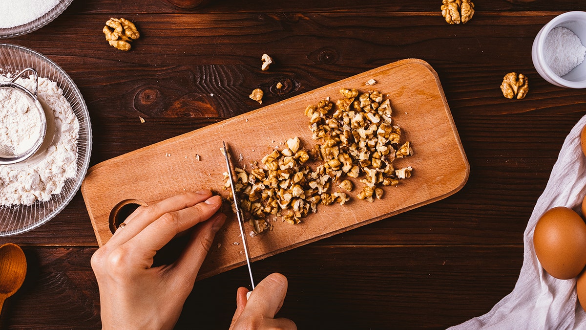Hand seen chopping walnuts on wood cutting board with knife