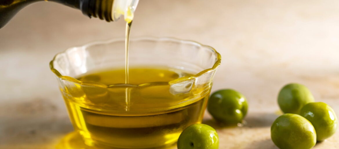 A daily dose of olive oil can cut your heart disease risk Close up of bottle pouring olive oil into bowl with olives sat beside it