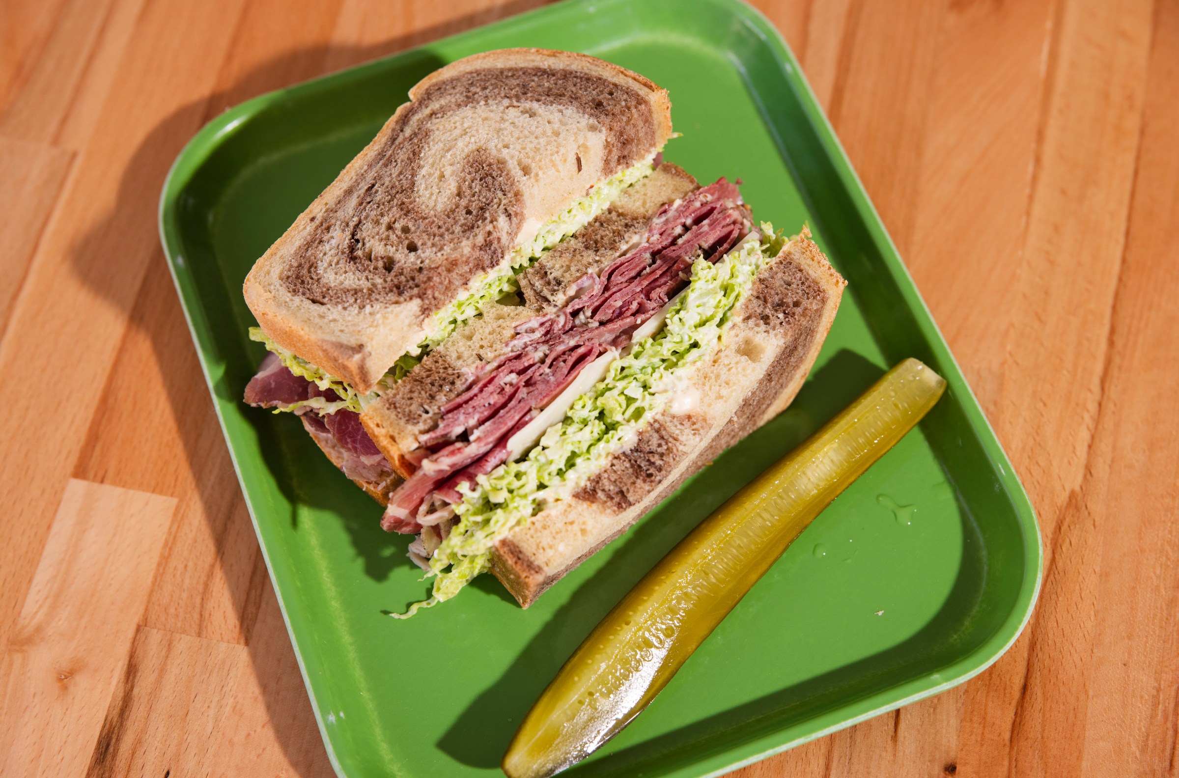 A corned beef sandwich and side pickle on a green tray at Dream Deli in Portland, Oregon.