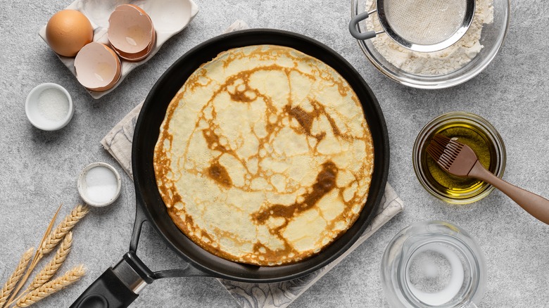 A crepe on a pan surrounded by ingredients