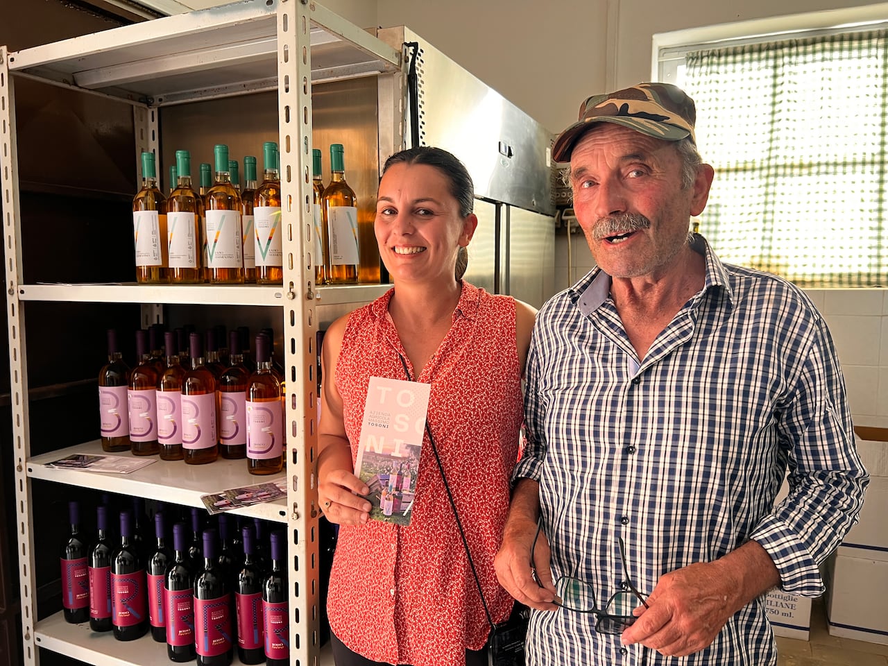 Two people stand beside shelves with wine bottles.