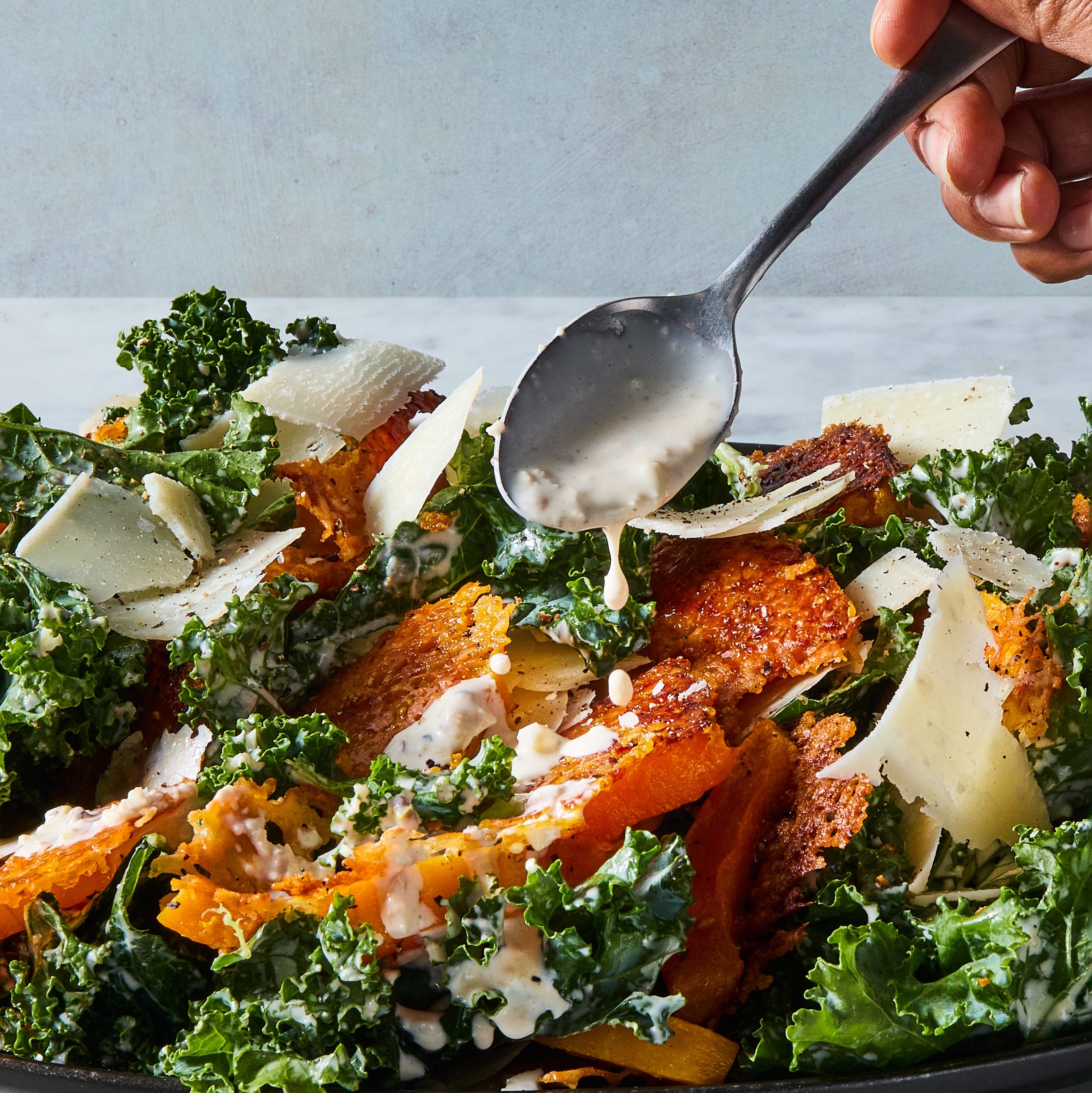 harvest caesar salad with squash croutons, parmesan, and caesar dressing drizzling over from a spoon