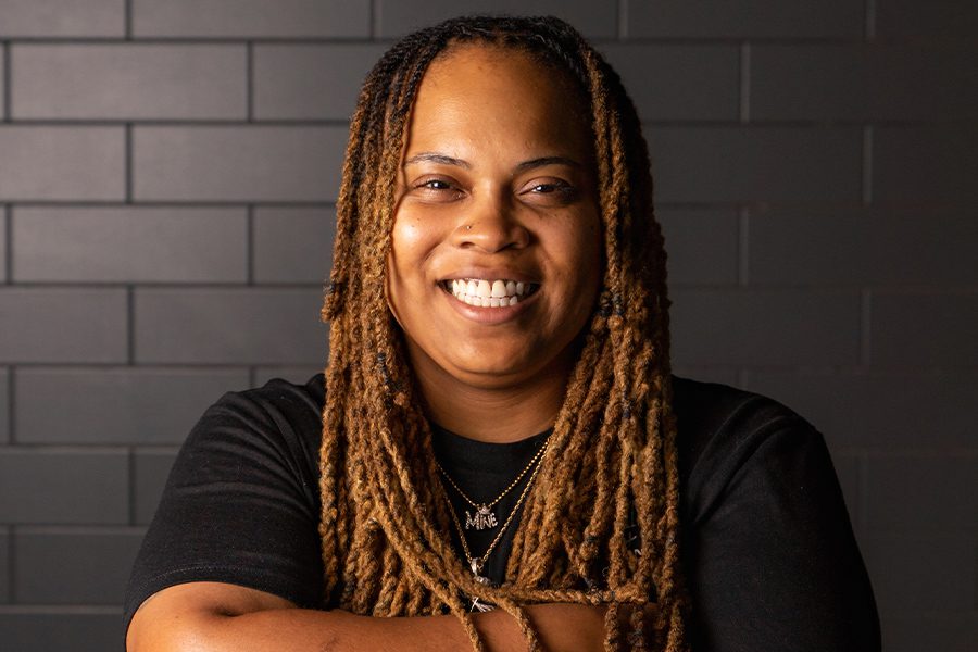 Food Network Champion to Keynote Game-Changing 51st Stafford Dinner Food Network Champion with long, light brown dreadlocks and a black t-shirt smiles in front of a dark tiled wall.