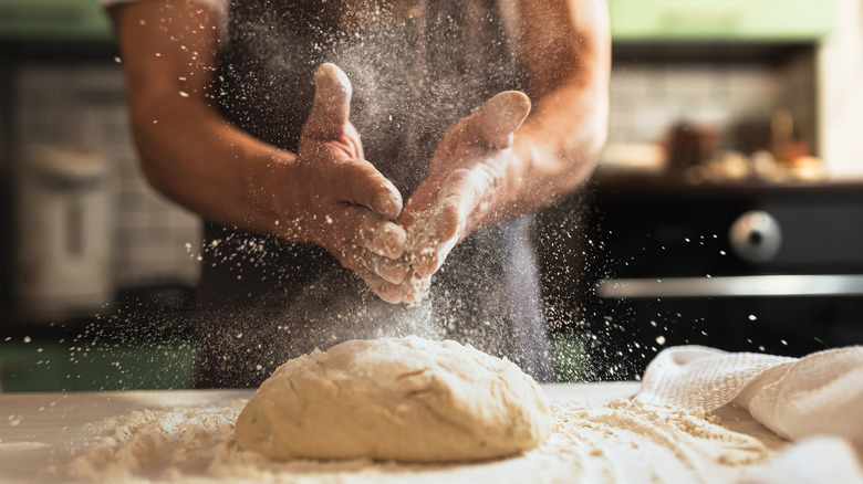 A man puts flour on his hands to prepare for working with bread dough
