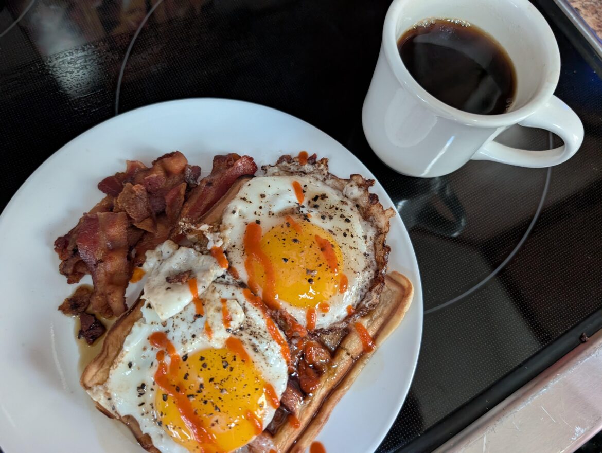Homemade waffle, bacon, extra dark maple syrup with two sunny side up eggs on top