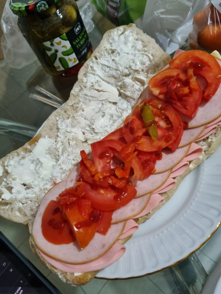 Gluttonous sandwich with creme cheese, salami, smoked turkey, tomatoes, pickles, sriracha and some slices cheese buried under allat.