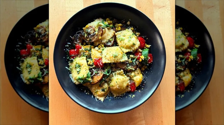Sweet corn ravioli with vegetables in black bowl