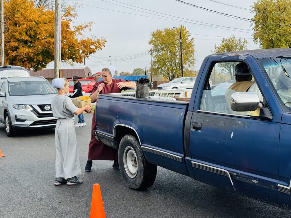 woman handing out carton of food next to truck