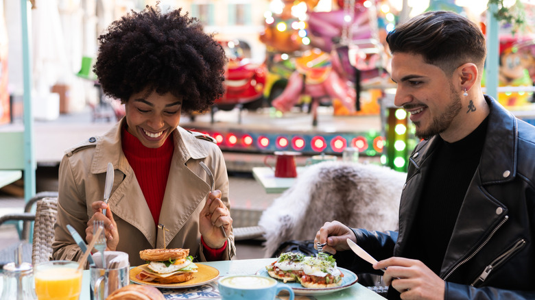Friends eating meal outdoors in front of fairground ride