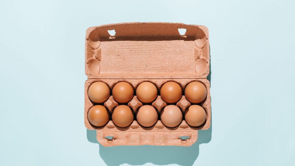 Holiday Cooking Prep: Here’s Exactly How Long Eggs Last in Your Fridge A carton of brown eggs against a blue background.