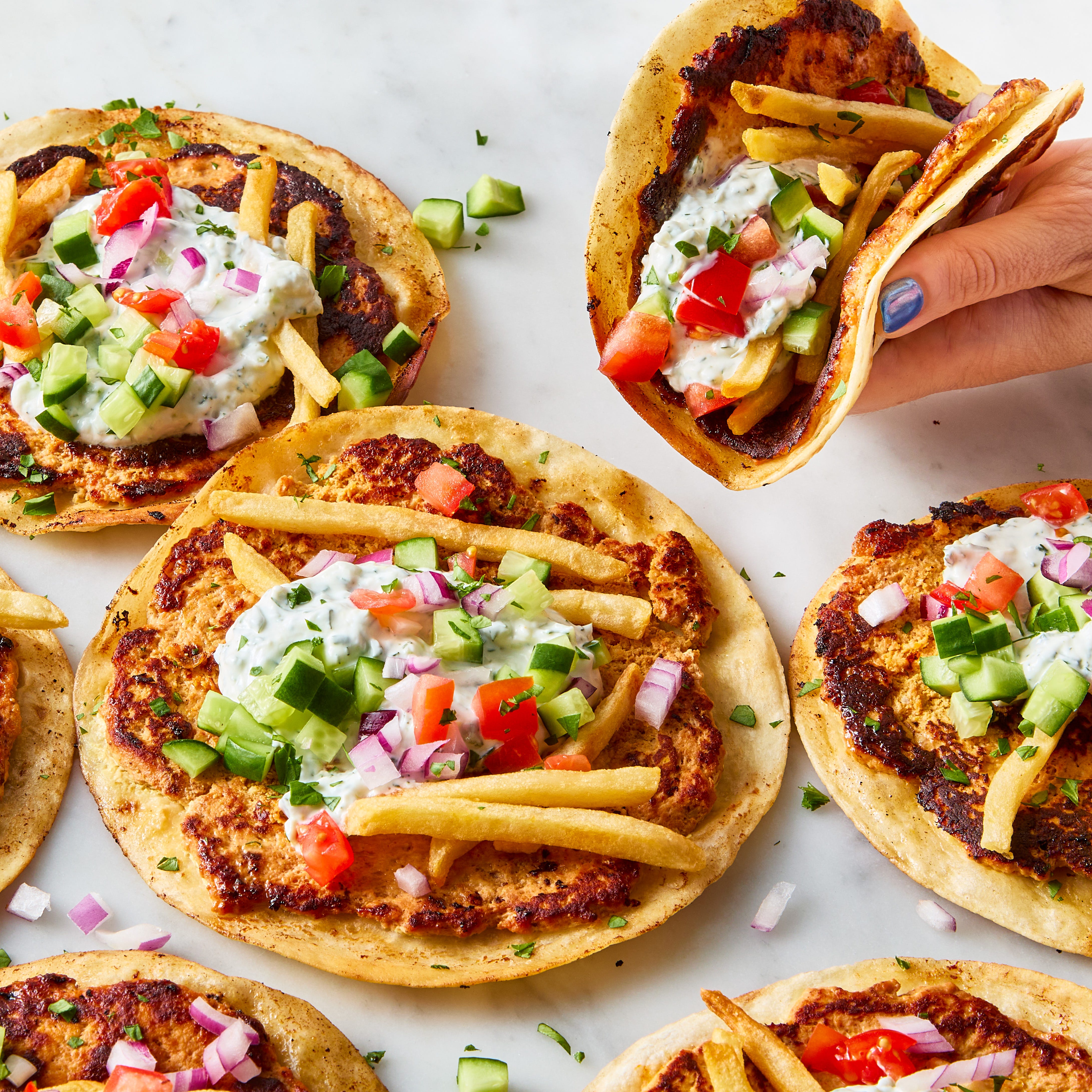gyros smash tacos topped with tzatziki, cucumbers, tomatoes, and french fries