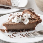 one slice of homemade chocolate pie on a white plate topped with Cool Whip and chocolate shavings