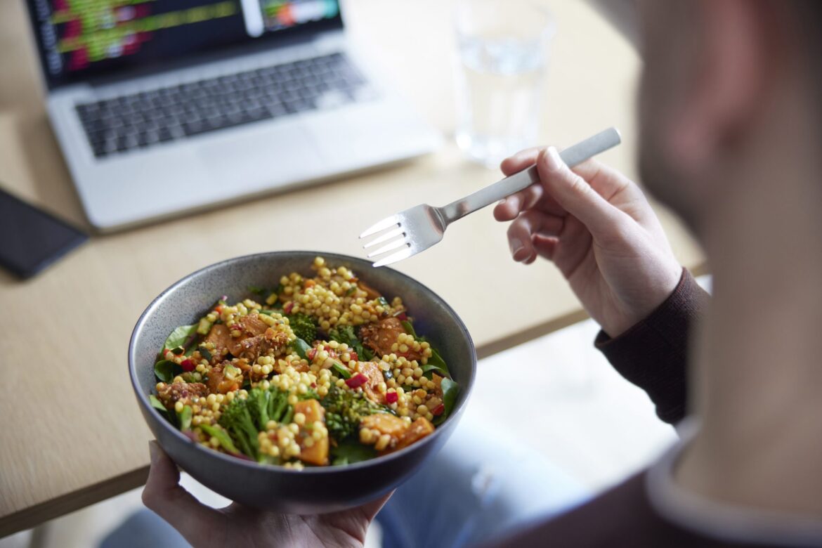 Vegan diet reduces carbon footprint by 46% in new study Close Of Man Eating Healthy Vegan Lunch At Office Deak Whilst Using Laptop