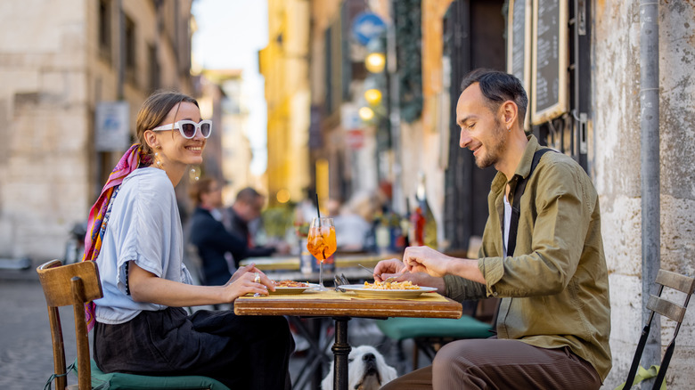 Two people sitting at a restaurant's outdoor table and eating in Europe