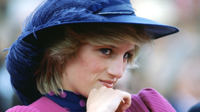 Diana, Princess of Wales holds her hand to her chin and smiles