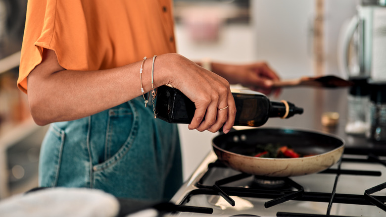person pouring olive oil into skillet at stovetop