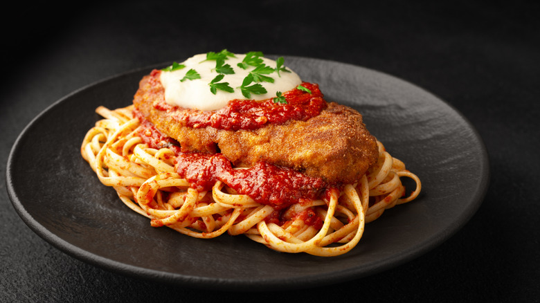 A plate of chicken Parmesan on bed of pasta noodles